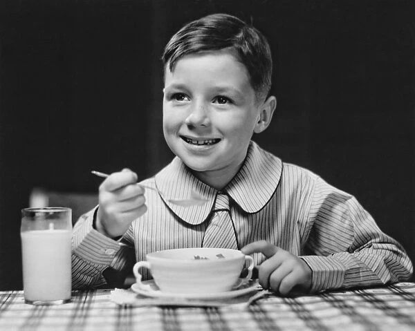 Elegant boy (6-7) eating at table, (B&W), portrait
