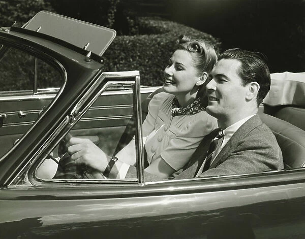 Elegant couple riding in in convertible car, (B&W)