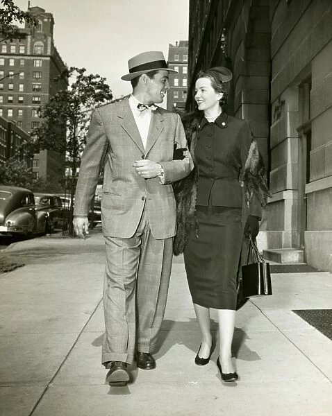 Elegant couple walking on sidewalk, (B&W)