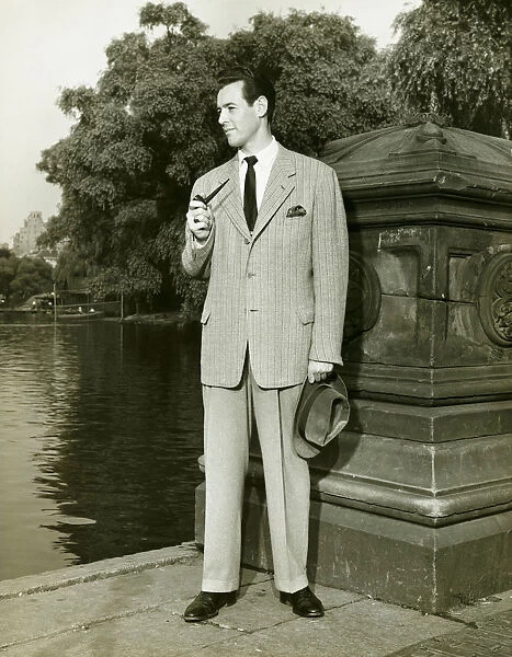 Elegant man smoking pipe by park lake, (B&W), portrait