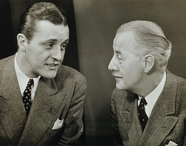 Two elegant men talking in studio, (B&W), close-up