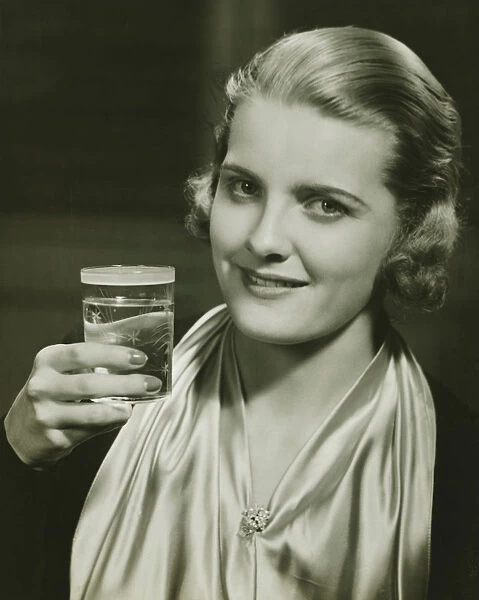 Elegant woman raising glass of water, posing in studio, (B&W), close-up, portrait