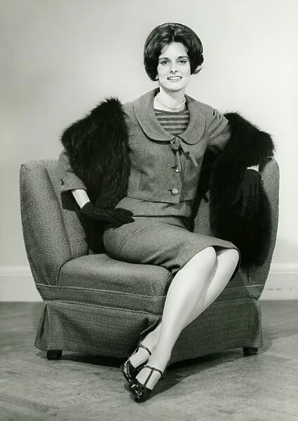 Elegant woman sitting on arm chair in studio, (B&W), portrait