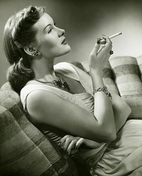 Elegant woman sitting on couch, smoking cigarette, (B&W)