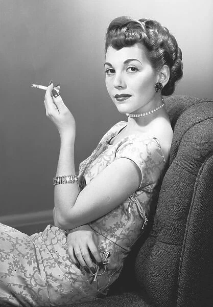Elegant woman smoking cigarette in studio, (B&W), portrait