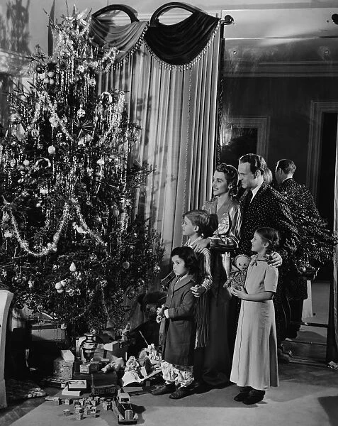 Family with three children (4-9) standing at Christmas tree, (B&W)