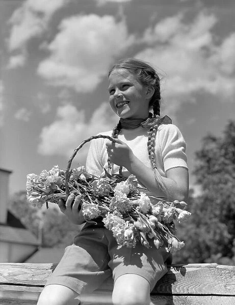 Farm girl with pigtails, sitting on fence, holding basket of flowers, smiling