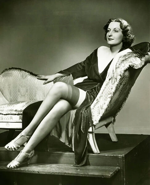 Fashionable woman in stockings sitting on chaise longue, (B&W), portrait