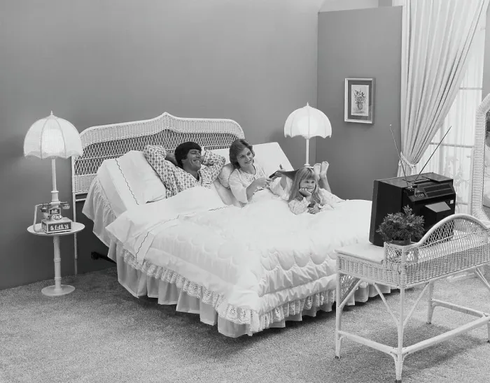Framed Print : Father and mother with daughter lying on bed watching tv, smiling