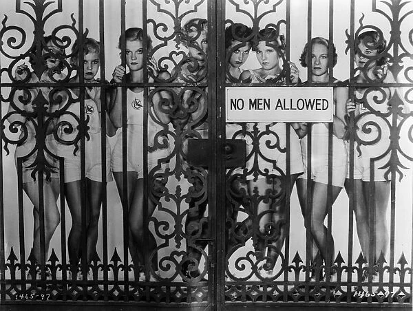 Fed Up. circa 1930: During filming in Hollywood girls pose behind wrought