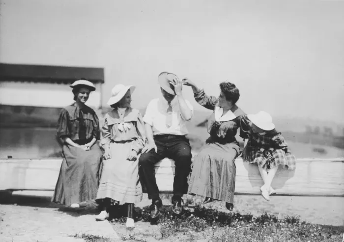 Framed Print : Fence Sitters; Three women, a man and a girl sit on a fence while one of the women Framed Print : Fence Sitters; Three women, a man and a girl sit on a fence while one of the women