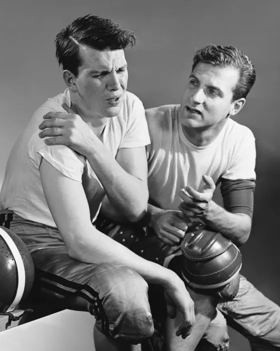 Framed Print : Football player holding sore shoulder; trainer sitting beside him Framed Print : Football player holding sore shoulder; trainer sitting beside him