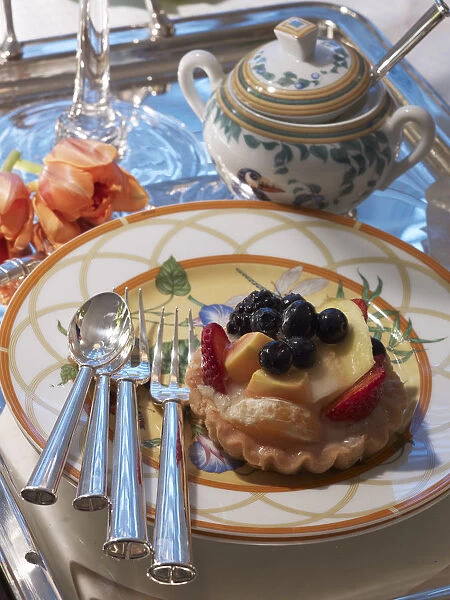 Fruit tart on a decorative plate with silver cutlery and a stylish ambience