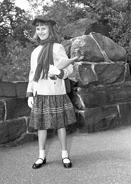Girl (12-13) holding book, posing by wall, (B&W), portrait