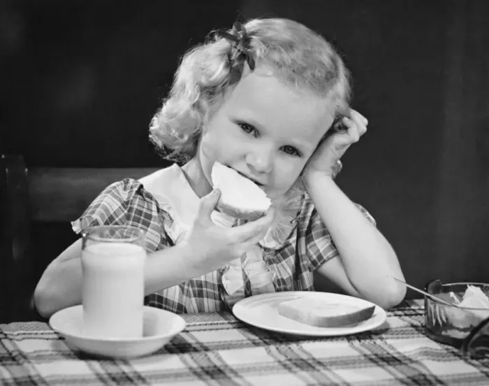 Framed Print : Girl (6-7) eating breakfast, resting head on hand, (B&W)