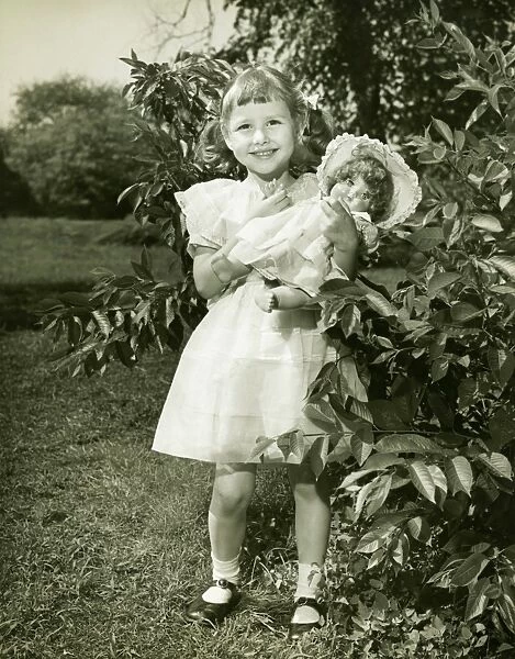 Girl (6-7) holding doll, posing in park, (B&W), (Portrait)