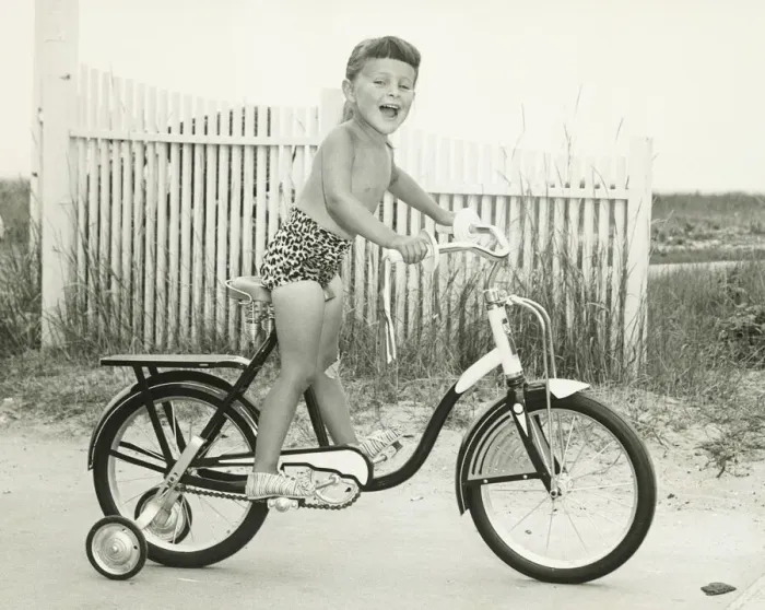Framed Print : Girl (6-7) riding bicycle with side wheels, (B&W) Framed Print : Girl (6-7) riding bicycle with side wheels, (B&W)