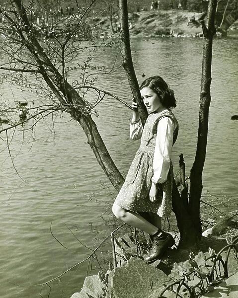 Girl (8-9) leaning on tree trunk by water, (B&W), elevated view