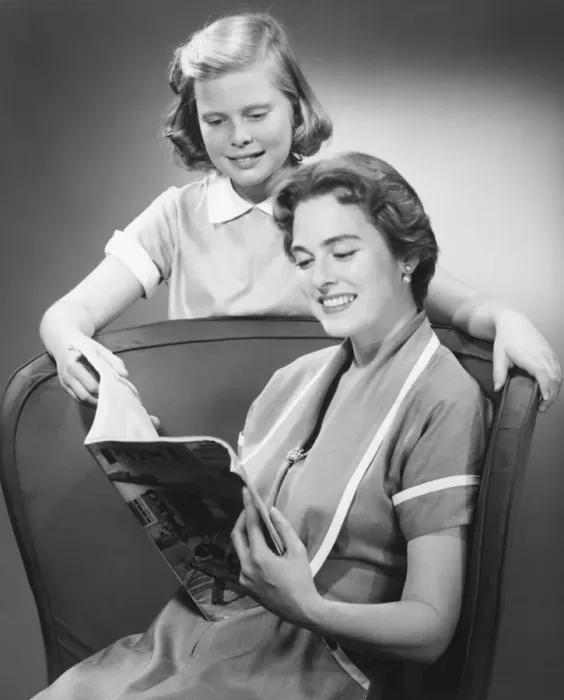Framed Print : Girl (8-9) standing at mother reading magazine, (B&W) Framed Print : Girl (8-9) standing at mother reading magazine, (B&W)