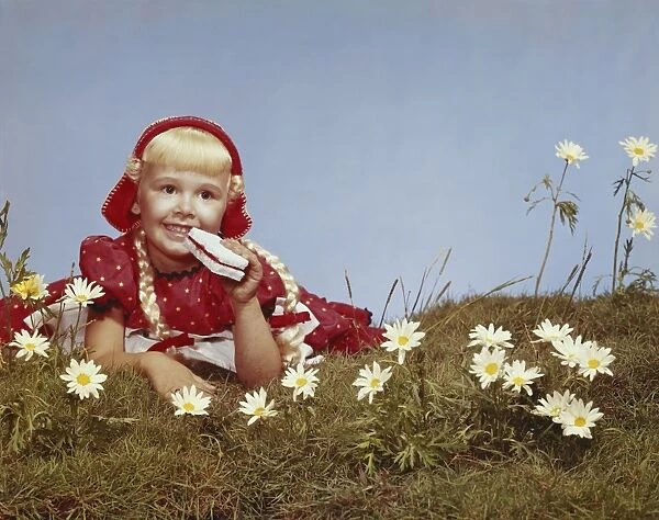 Girl lying in meadow eating bread and jam, smiling