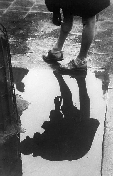 Saggy. circa 1930: A girl pulling up her stockings is reflected in a puddle