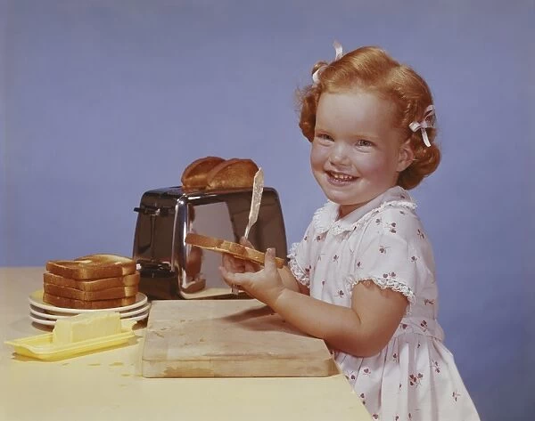 Girl spreading butter on toast, smiling, portrait