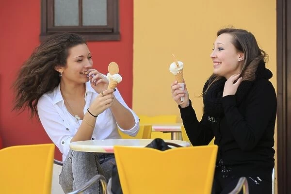 Two girlfriends, teenagers, eating ice cream from cone on the terrace an ice cream parlour, Menton, Alpes-Maritimes, Provence-Alpes-Cote dAzur, France