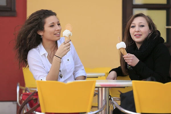 Two girlfriends, teenagers, eating ice cream from cones on the terrace an ice cream parlour, Menton, Alpes-Maritimes, Provence-Alpes-Cote dAzur, France