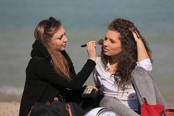 Two girlfriends, teenagers, sitting on the beach, applying makeup on each other, Menton, Alpes-Maritimes, Provence Alpes, France