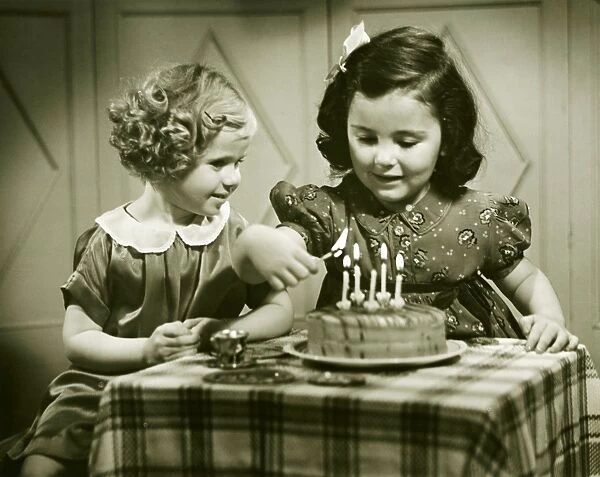Two girls (3-4), (4-5) sitting at small table with birthday cake, (B&W)