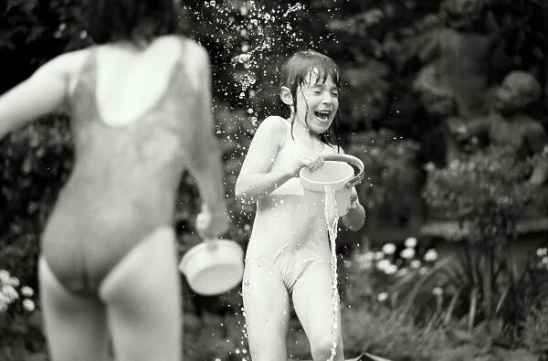 Two girls (7-9) in swimwear having water fight in garden (B&W)