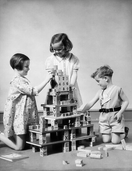 Two girls and one boy playing with alphabet building blocks constructing multi story structure
