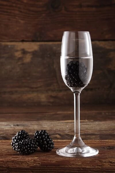 Glass of Blackberry schnapps with Blackberries (Rubus sectio Rubus) in front of rustic wood