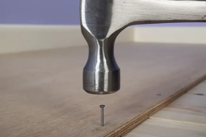 Framed Print : Hammering a ring-shank nail in to plywood on the floor
