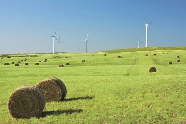 Hay bales in a green field with wind turbines against a blue sky