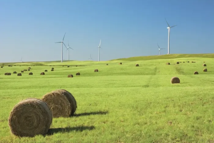 Framed Print : Hay bales in a green field with wind turbines against a blue sky
