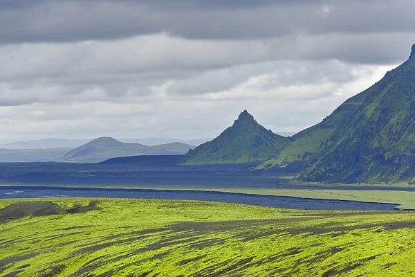 Hills covered with moss in front of an area with black sand and a pointed mountain, view from the road into the Pakgil or Thakgil Valley, Iceland