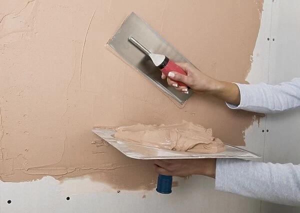 Holding a plastering hawk and spreading plaster onto a wall with a trowel