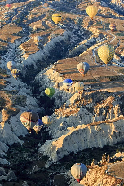 Hot air balloons flying above rock formations in Red Valley, Goreme National Park, Goreme, Cappadocia, Anatolia, Turkey