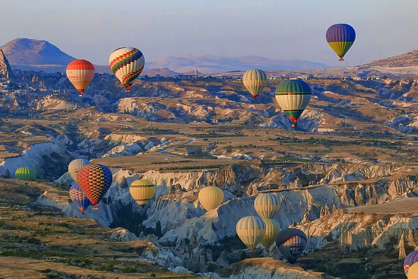 Hot air balloons flying above rock formations in Red Valley, Goreme National Park, Goreme, Cappadocia, Anatolia, Turkey