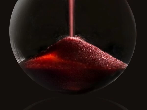 hourglass. A simple and elegant macro photo of red sand pouring into the