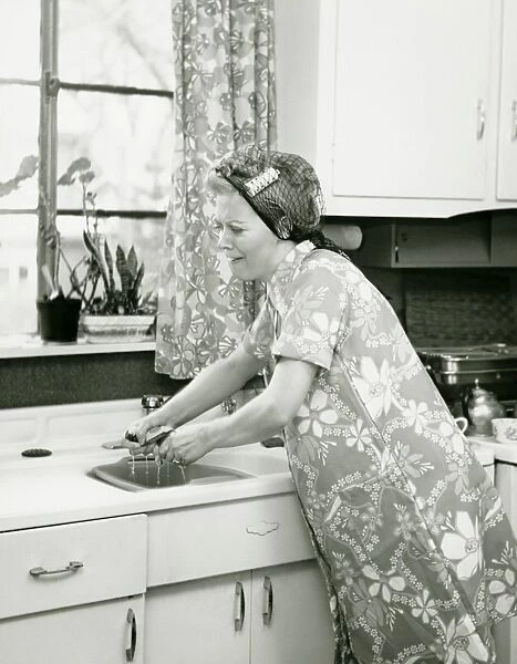 Housewife doing dishes at kitchen sink, (B&W)