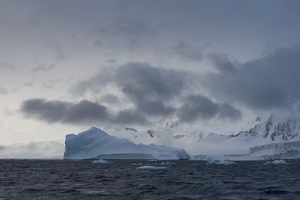 Iceberg in a fjord with mountain scenery and a cloudy sky, Gerlache Strait, Antarctic Peninsula, Antarctica
