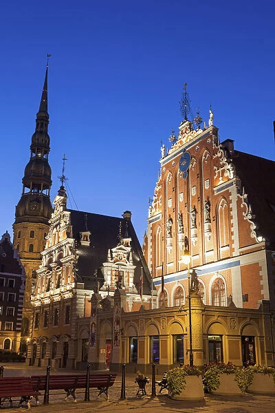 Latvia, Riga, Illuminated House of the Blackheads and St. Peters Church against blue sky