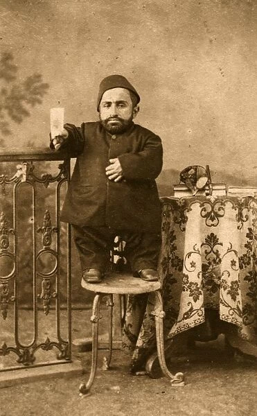 A Leg Up. circa 1890: A dwarf stands on a stool to have his portrait photographed