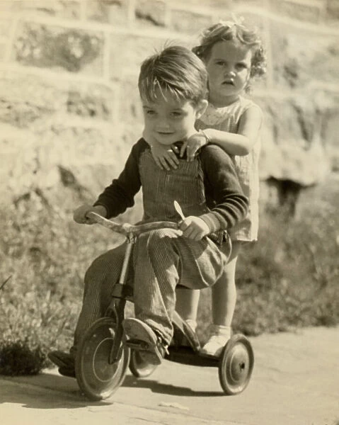 Little boy giving little girl ride on tricycle