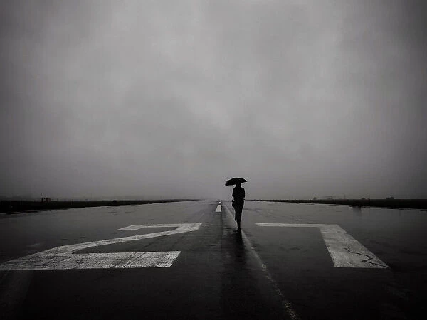 Lone woman with umbrella on empty runway 27 left at Tempelhof Airport in Berlin on a rainy day