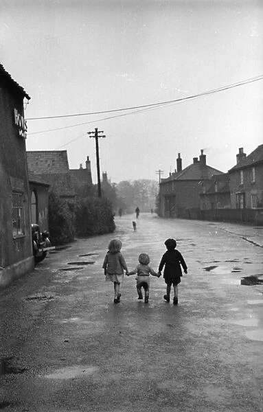 Its A Lonely Road; Three children walk hand in hand down the main street of the village