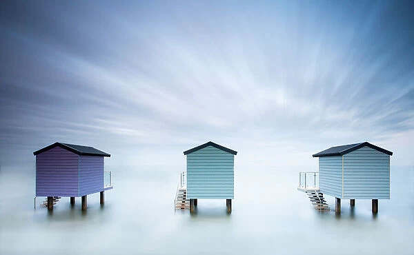A long exposure shot of 3 beach huts at high tide