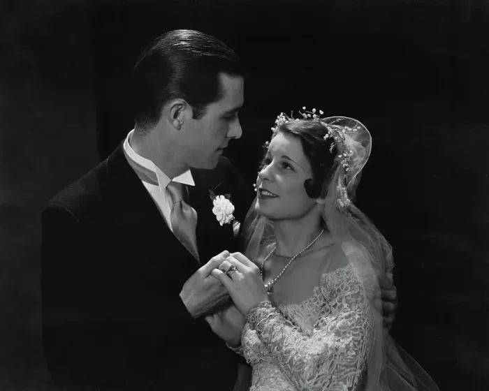 Framed Print : Love Is. A groom and bride, her veil lifted, in a black suit